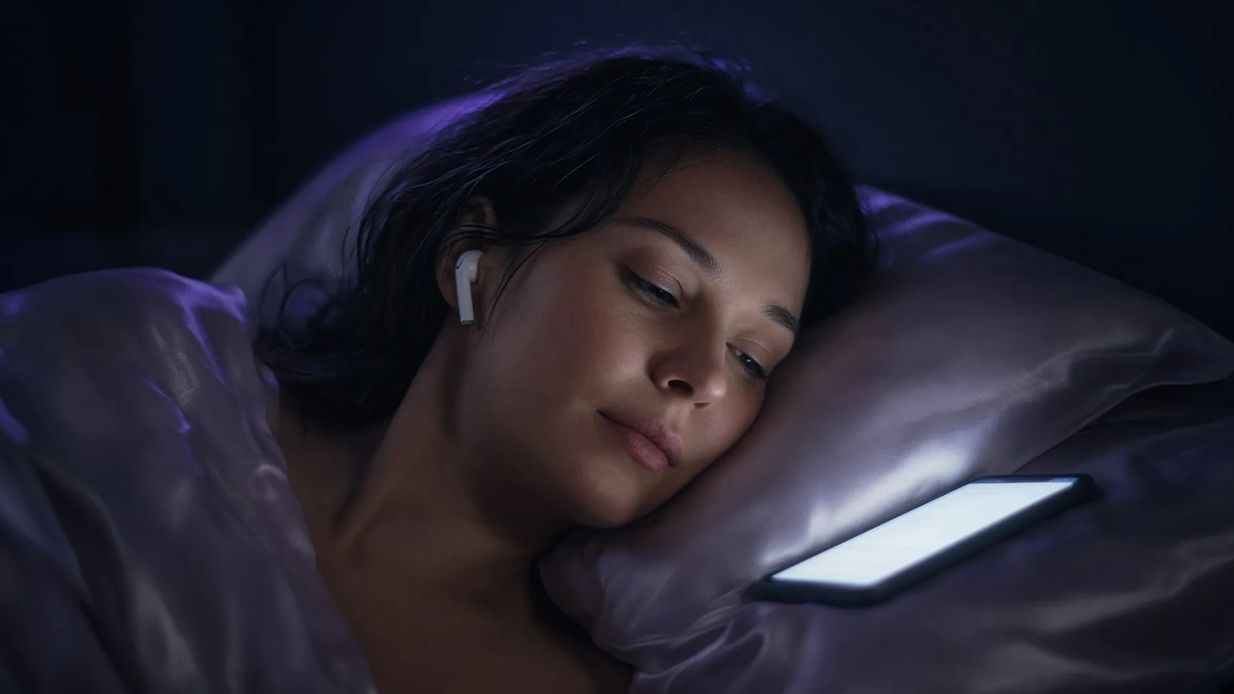 Woman with earbuds on a night bed taking an AI boyfriend voice call, XXXFuel